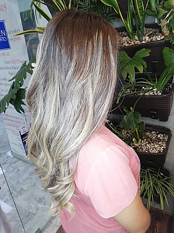 Cabello largo platino con raíz difuminada, de espaldas junto a la jardinera